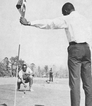 a caddy holds the flag as a golfer lines up a putt